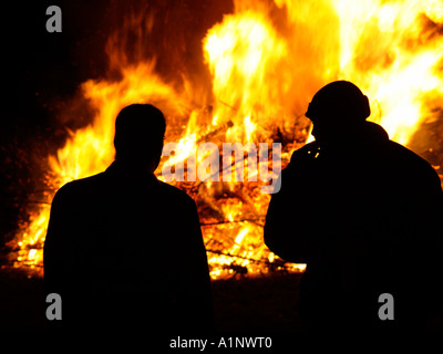 zwei Männer, die Silhouette vor ein riesiges Feuer Feuer aus der Verbrennung von alten Weihnachtsbäume Stockfoto