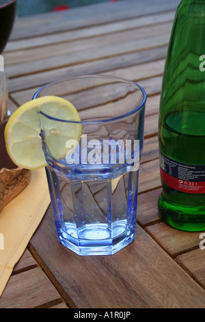 Glas Mineralwasser mit Zitronenscheibe auf einem Holztisch neben einer grünen Flasche. Stockfoto