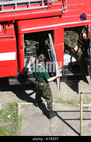 Feuerwehrmann in grüner Uniform öffnet die Tür eines roten Feuerwehrwagens und bereitet sich auf die Aktion in Kiew, Ukraine, vor. Stockfoto