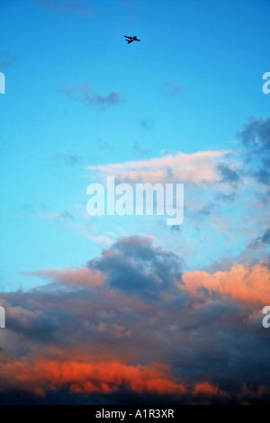 Das Flugzeug fliegt über einen leuchtend blauen Himmel mit verstreuten Wolken bei Sonnenuntergang. Stockfoto