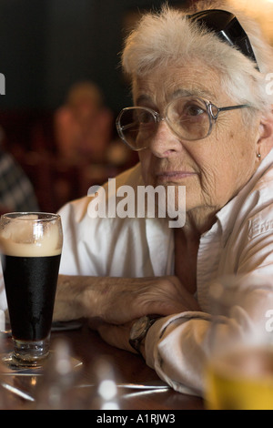 Es absetzen zu lassen: eine ältere Frau wartet, während ihr halbes Pint Guinness Stout setzt sich vor dem Trinken Stockfoto