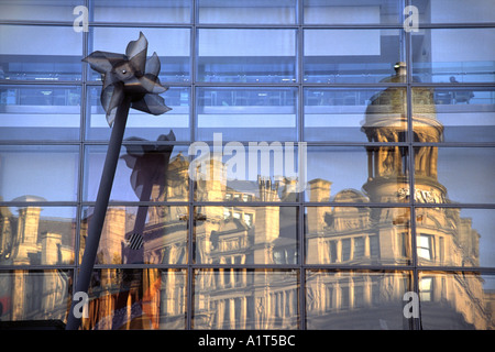 Das Dreieck spiegelt sich in den Fenstern von Selfridges, Exchange Square, Manchester UK, mit einer "Windmühle" Skulptur im Vordergrund Stockfoto