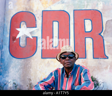 Mann mit Sonnenbrille sitzt vor einem CDR-Wandgemälde in Havanna, Kuba. Stockfoto