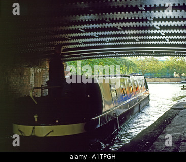 Ein langes Schmalboot, das unter einer alten Eisenbrücke auf der Kreuzung Grand Union und Regents Canal bei Little Venice in London, England, Großbritannien, FÄHRT, KATHY DEWITT Stockfoto