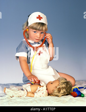 Ein junges Mädchen in einem Krankenschwestern-Kostüm spielt mit ihrer Puppe und ein Stethoskop Stockfoto