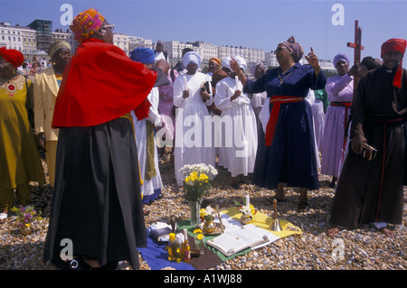 CHRISTLICHE TAUFE ZEREMONIE STATT IM MEER IN BRIGHTON MENSCHEN IN BUNTEN GEWÄNDERN SAMMELN AM STRAND GEKLEIDET Stockfoto