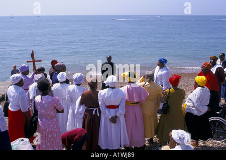CHRISTLICHE TAUFE ZEREMONIE STATT IM MEER IN BRIGHTON MENSCHEN IN BUNTEN GEWÄNDERN SAMMELN AM STRAND GEKLEIDET Stockfoto