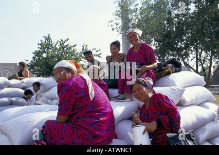 GRUPPE VON FRAUEN TRAGEN KOPFTUCH PINK FLORAL PRINT KLEIDER SITZT AUF STAPEL SÄCKE BROT IN TASCHKENT MARKT 1998 VERKAUFT Stockfoto