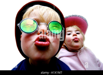 fünf Jahre alten Jungen tragen Witz Brille und zwei Jahre altes Mädchen mit Hut beide schmollend in die Kamera vor weißem Hintergrund Stockfoto