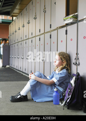 Elementare Schülerin am Boden gegen Schule Schließfächer Stockfoto