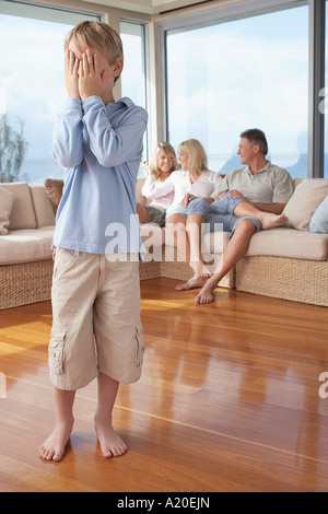 Junge stand, versteckt Gesicht von Familie im Hintergrund Stockfoto