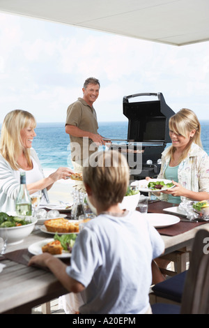 Familie herumsitzen Tisch draußen essen Grillen, Vater am Grill Grillen Stockfoto
