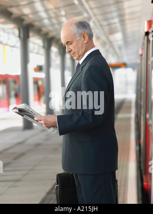 Geschäftsmann lesen Zeitung am leeren Bahnhof, Seitenansicht Stockfoto