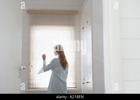 Frau spähte durch Jalousien stehen am Fenster, halbe Länge Stockfoto