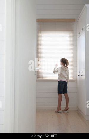 Junges Mädchen spähte durch Jalousien stehen am Fenster, in voller Länge Stockfoto