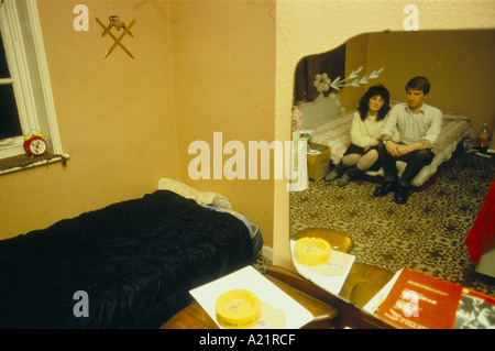 OBDACHLOSEN PAAR IN SPIEGELBILD SITZT AUF BETT MIT BRUDER EIN ZIMMER TEILEN Stockfoto