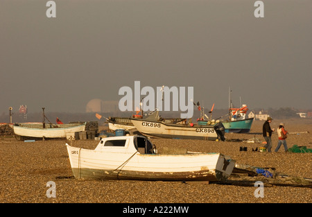 Menschen zu Fuß durch kleine Fischerboote am Strand von Aldeburgh. Kernkraftwerk Sizewell B ist am Horizont links von der Mitte Stockfoto