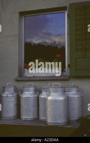 Große metal Molkerei Milch Dosen Website am Tisch vor dem Fenster mit Blumenkasten reflektierende Sunrise in einer kleinen Stadt in der Schweiz Stockfoto