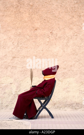 ein marokkanische Mann trägt einen traditionellen Jellaba sitzt auf der Straße neben der alten Medina Wand Stockfoto