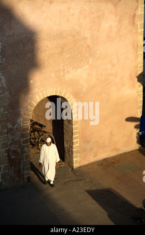 ein traditionell gekleidet Marokkanische Mann Spaziergänge durch einen Torbogen von der alten Stadtmauer der Medina in Essaouira mit dramatischen Licht und Schatten. Stockfoto