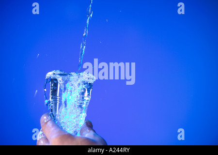 Wasser gegossen in Einweg-Becher vor blauem Hintergrund Stockfoto