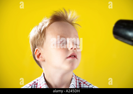 Blonde junge im Alter von 5-7 Jahren gegen gelbe Studio-Hintergrund lustige Grimassen und dabei seine Haare Schlag getrocknet. Stockfoto