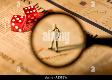 Miniatur-Geschäftsmann durch Lupe auf Finanzzeitung mit zwei Würfeln im Hintergrund stehend gesehen Stockfoto