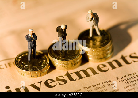 Miniatur-Geschäftsleute auf Stapel von Münzen auf Finanzzeitung mit Investitionen Überschrift stehen Stockfoto