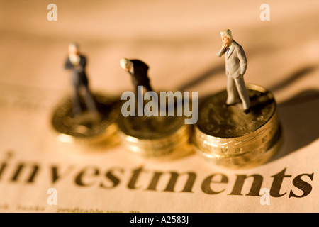 Miniatur-Geschäftsleute auf Stapel von Münzen auf Finanzzeitung mit Investitionen Überschrift stehen Stockfoto