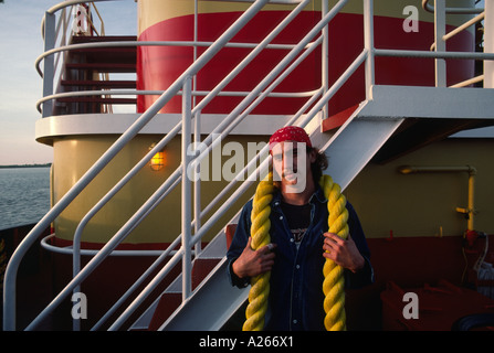 Nach vorne gerichtete Porträt einer schweren schnauzbärtige Deck Hand in ein rotes Halstuch posiert mit gelben Seil in der Nähe von Schiffen Geländer tragen. Stockfoto