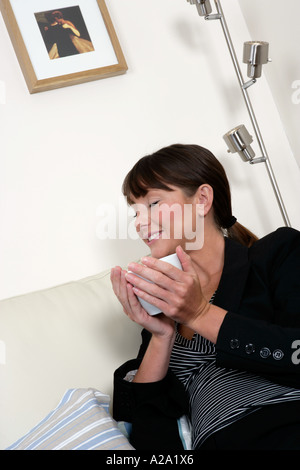 junge Frau hält eine Tasse Kaffee genießen das Aroma mit ihren Augen geschlossen Stockfoto