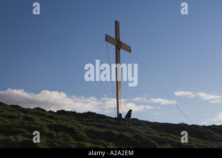 Mann, der am Fuße eines großen Holzkreuzes steht, das hoch auf einem ländlichen Hügel in Eastertime und am tiefblauen Himmel errichtet wurde - Otley Chevin, Yorkshire, England, Großbritannien. Stockfoto