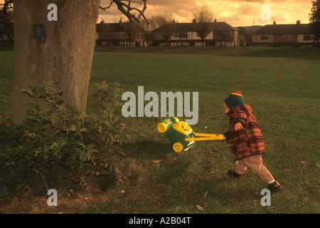 Kleiner Junge mit einem Spielzeug Rasenmäher, vorgibt, das Mähen In einem Park. Stockfoto