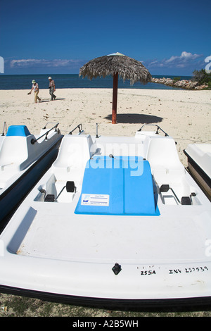 Tretboot Boot, Sonnenschirm und Menschen zu Fuß auf einem Strand, Guardalavaca, Provinz Holguin, Kuba Stockfoto