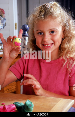 Kaukasische Mädchen 8-10 Jahre alte Stück Teig Ton-Gesicht, genießen Sie ruhige Zeit am Tisch ziemlich niedlich locken Grübchen gekräuselt Haar halten POV Stockfoto