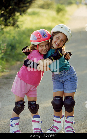 Zwei junge Mädchen umarmten einander und das Lachen als sie Rollerblade tragen Helme und Schutz-pads Stockfoto