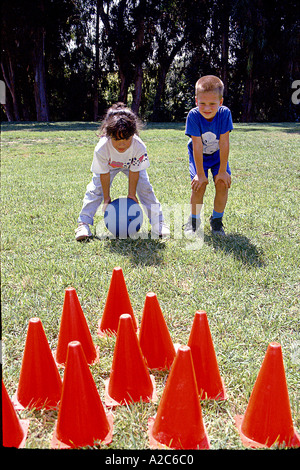 zwei Kinder 5-7 Jahre alte junge Mädchen spielen kooperativen Outdoor POV Kiddies Rasen-Bowling Rollenkugel richtet sich an vielfältigen ethnischen ethnische Vielfalt Stockfoto