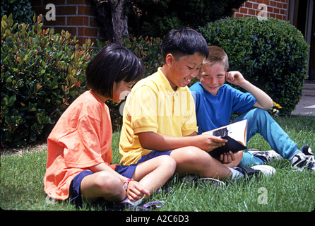 Junge Mensch Menschen Tween Tweens außerhalb Gras Buch lesen sitzen gemeinsam Vielfalt rassisch unterschiedlichen Glücklich lächelnde multikulturellen © Myrleen Pearson Stockfoto