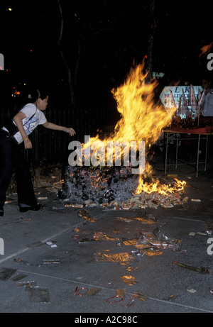 Eine Frau, die während des Festivals des hungrigen Geistes Papiergeld in ein Lagerfeuer in Singapur zu werfen Stockfoto