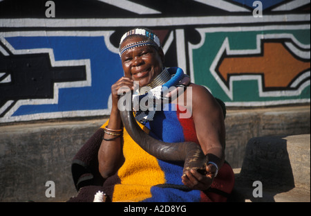 Ndebele Frau bläst ein Kudu horn vor Finger gemalt Haus, Botshabelo Ndebele Dorf, Südafrika Stockfoto