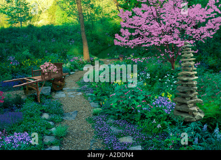 Zen-artige Schatten Garten hat große Hand gefertigte Cairn als Kunst und eine Schubkarre voll von neuen Pflanzen zum Anpflanzen Stockfoto