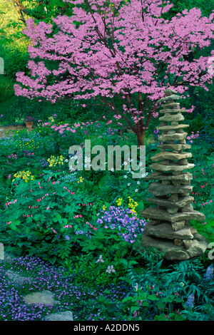 Rock Cairn steht in einheimischen Wildblumen Garten mit rosa Hartriegel Baum im Hintergrund Stockfoto