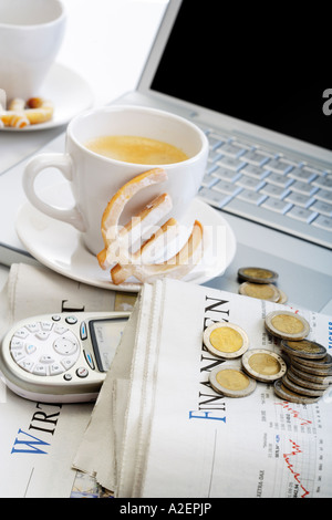 Tasse Kaffee, Euro Cookie, Münzen, Zeitung und Mobile vor laptop Stockfoto