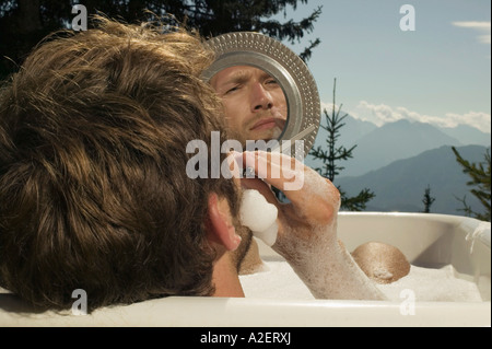 Junger Mann liegend in Badewanne, rasieren Stockfoto
