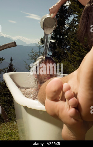 Junger Mann in der Badewanne liegend, junge Frau gießt Wasser auf Mann Stockfoto