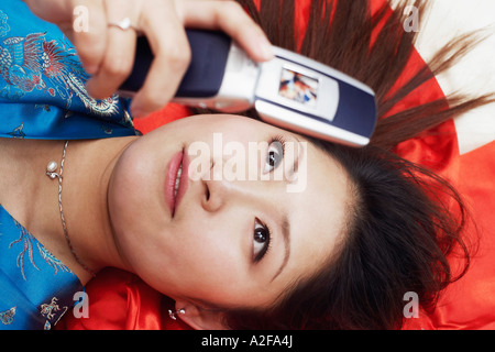 Erhöhte Ansicht einer jungen Frau auf dem Rücken halten eines Handys liegt Stockfoto