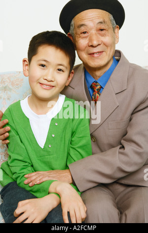 Bildnis eines Knaben mit seinem Großvater lächelnd auf einer Couch sitzend Stockfoto