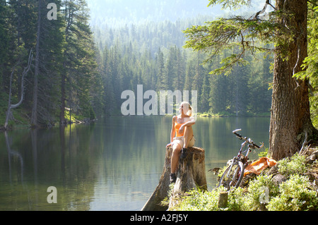 Junge Frau sitzend auf Baumstamm und wegsehen Stockfoto
