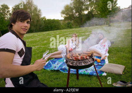 Junger Mann Grillen junge Frauen im Hintergrund Stockfoto