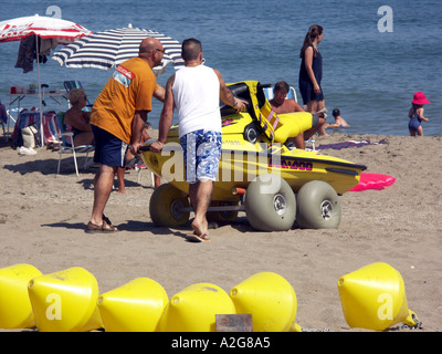 Männer schieben Jet Ski auf einem Wagen über den Strand, La Cala de Mijas, Mijas Costa, Costa Del Sol, Spanien, Europa, Stockfoto